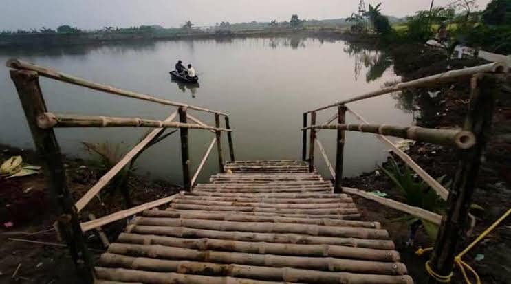 A bamboo jetty leading down to a pond with a small rowing boat